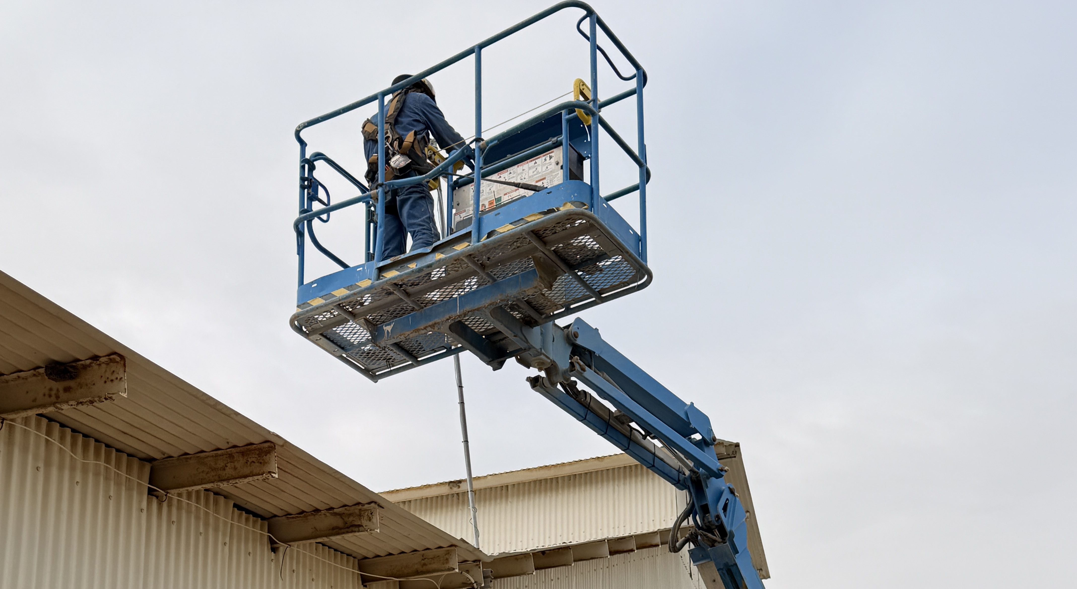 Worker on a scissor lift wearing a full-body fall-protection harness performing elevated work
